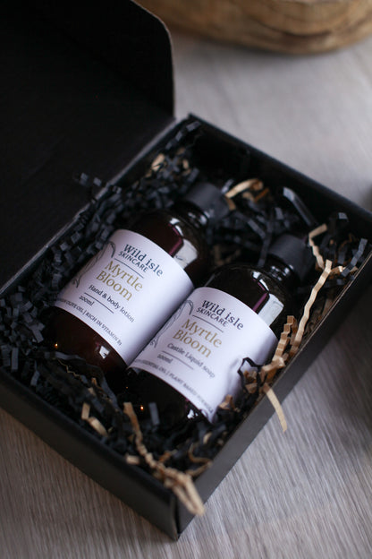 Three bottles of 'Myrtle Bloom' hand and body lotion in a black gift box on a wooden surface.